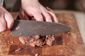 Male hands cutting cooked meat beef on a wooden board