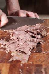 Male hands cutting cooked meat beef on a wooden board