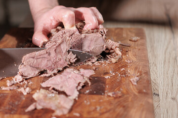 Male hands cutting cooked meat beef on a wooden board