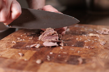 Male hands cutting cooked meat beef on a wooden board