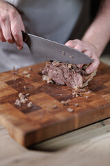Male hands cutting cooked meat beef on a wooden board