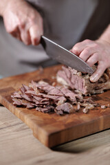 Male hands cutting cooked meat beef on a wooden board