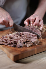 Male hands cutting cooked meat beef on a wooden board