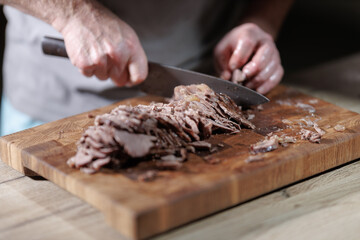 Male hands cutting cooked meat beef on a wooden board