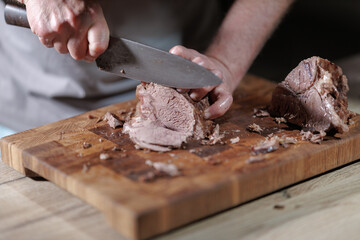 Male hands cutting cooked meat beef on a wooden board