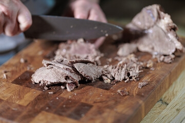 Male hands cutting cooked meat beef on a wooden board