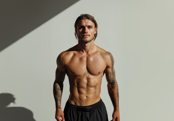 Fototapeta premium Tanned athletic male with tattoos standing confidently in a well-lit studio showcasing a fit physique during a fitness photoshoot