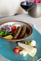 Grilled Adana kebab with a side of fresh vegetables and a glass of red wine