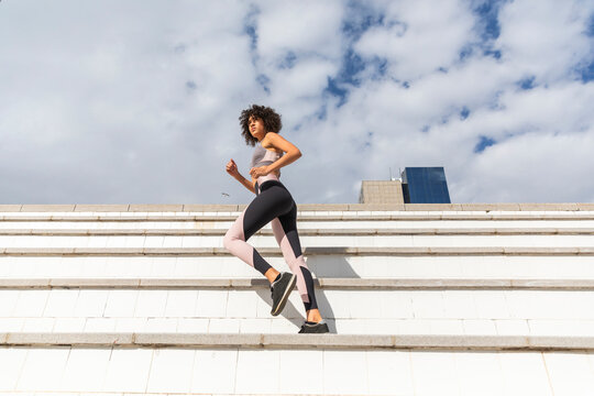 Runner practicing exercise near steps under cloudy sky