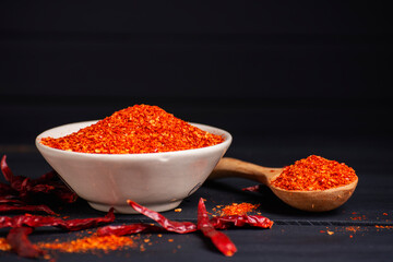 Chili powder, dried chilies, spicy condiments in a bowl placed on a table, dark background.