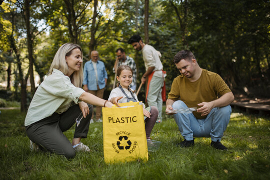 Socially inclusive group of volunteers putting plastic waste in recycling bag