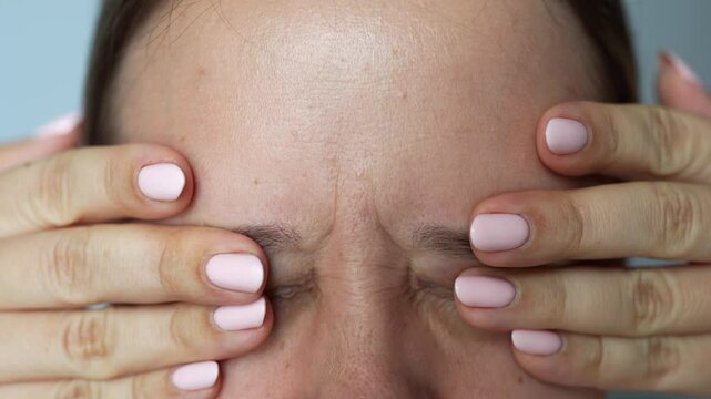 Young caucasian blonde woman covering her eyes pressing on them with hands suffering from eye pain on gray background. Photophobia, painful sensitivity to bright light. Ophthalmology concept