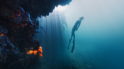 Freediver gracefully descending along a vibrant reef wall bathed in sun rays. Raja Ampat, Indonesia