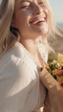 Close up of a beautiful young blonde woman holding a bouquet of flowers and smiling. She is joyful.