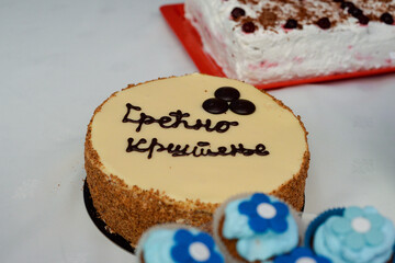 A round light brown cake with Happy Baptism written on it in Cyrillic Serbian script