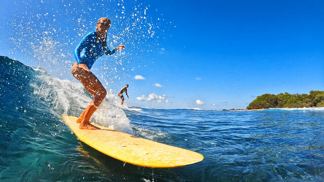 Young athletic woman in a blue swimsuit is riding a yellow surfboard on ocean waves. Maldives