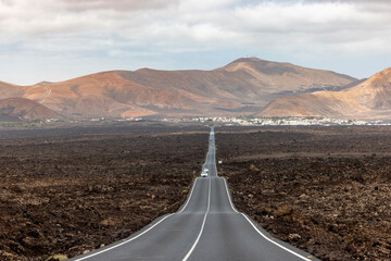 View of an endless straight road in Lanzarote, Yaiza, Spain, featuring the volcanic landscape of Timanfaya.
