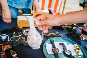 Hand holding a vase at a flea market with various items on the table.