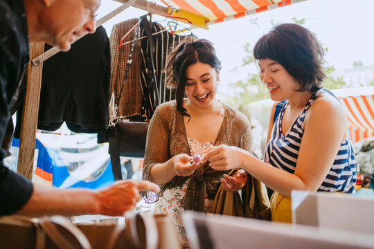 Young women and a senior man interacting at an outdoor flea market during the day.