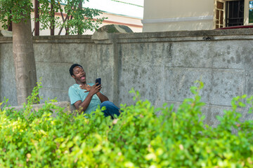 African American man siting in a garden using phone.