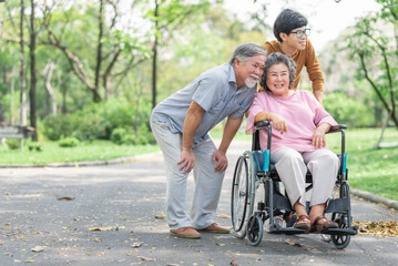 Happy Asian senior couple and son smiling outside in the park while woman sitting in wheelchair