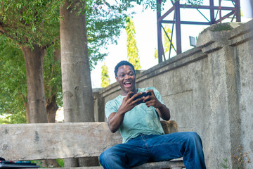 African American man siting in a garden using phone.