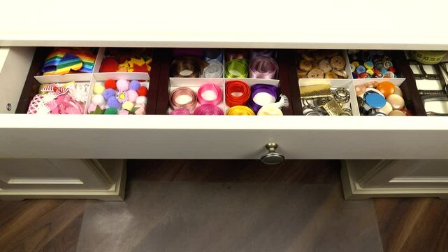 Desk drawer with clothing accessories for sewing and needlework is pushing out.  Organizing and storing things in the house. 