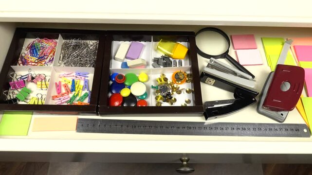 Stationery and office supplies are laid out in an open drawer of a white desk. Organizing and storing things in the house