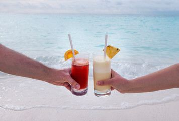 A close-up of a male and a female hands holding two glasses with cocktails