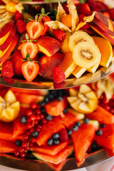 Ein farbenfrohes Obstbuffet auf einer zweistöckigen Etagere, dekoriert mit frisch geschnittenen Früchten wie Erdbeeren, Kiwi, Melone, Physalis und Beeren. 