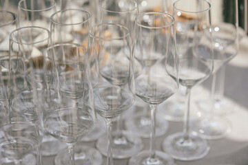 Eine Sammlung leerer, eleganter Weingläser, die dicht nebeneinander arrangiert sind und im Sonnenlicht schimmern. Die Szene wirkt vorbereitet und vermittelt eine festliche Stimmung.