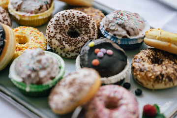 Eine Auswahl an Donuts und Muffins, dekoriert mit bunten Streuseln, Schokolade und Zuckerglasur, arrangiert auf einem Tablett. Die Leckereien wirken süß und einladend, perfekt für eine Party. 