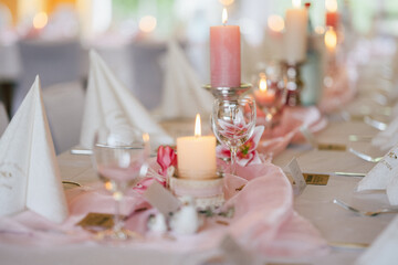 Eine festlich gedeckte Tafel mit rosa Tischdeko, Kerzen in verschiedenen Größen und gefalteten Stoffservietten. Die Atmosphäre wirkt elegant und romantisch, ideal für eine Hochzeit oder eine Feier.