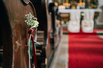einem roten Band, im Hintergrund ein roter Teppich, der zum geschmückten Altar führt. Die Szene...