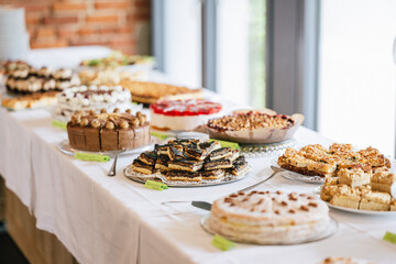 Ein reichhaltiges Kuchenbuffet mit verschiedenen Torten und Kuchen, darunter Schokoladentorte, Obstkuchen und Sahnetorten. Die Leckereien sind auf einer weiß gedeckten Tafel angerichtet.