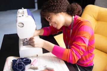 Young African woman working at sewing machine. Charming black girl in red sweater
