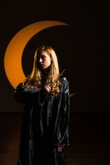 A red-haired woman magician casts a spell with a magic wand against the backdrop of a crescent...