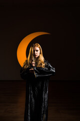 A red-haired woman magician casts a spell with a magic wand against the backdrop of a crescent...