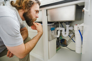 Man with hand on chin examining kitchen sink at home