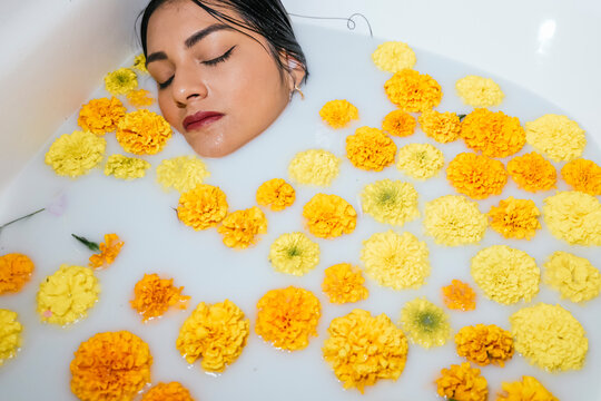 Relaxed woman in bathtub surrounded by marigold flowers