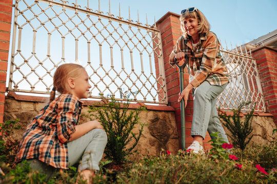 Smiling girl gardening with grandmother using shovel in back yard