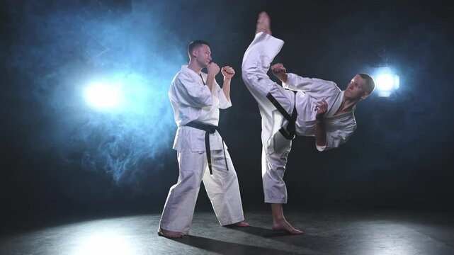 Martial arts masters on dark background. Strong man fighters in white kimono for karate martial arts fighting training in black gym. Karate fighters training punches kicks practicing fight sparring