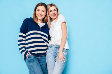 Two young beautiful smiling brunette hipster female in trendy summer clothes. Lovely women posing on blue background in studio. Positive models having fun. Cheerful and happy. isolated