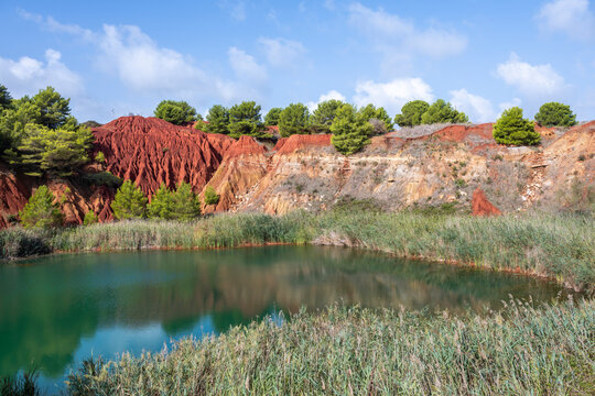 Red cliffs and a tranquil lake at Cava di Bauxite in Otranto, Apulia, Italy