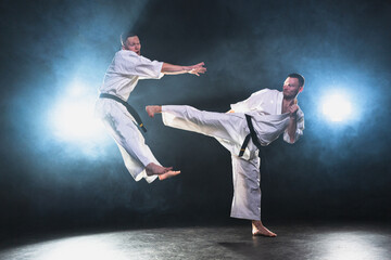 Martial arts masters on dark background. Strong man fighters in white kimono for karate martial arts fighting training in black gym. Karate fighters training punches kicks practicing fight sparring © Юлия Завалишина
