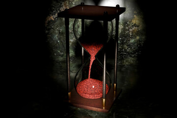 Antique hourglass with red sand and dark background.