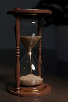 Wooden hourglass with sand on a desk indoors.