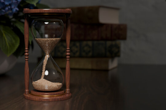 Wooden sandclock on a table with books in the background.
