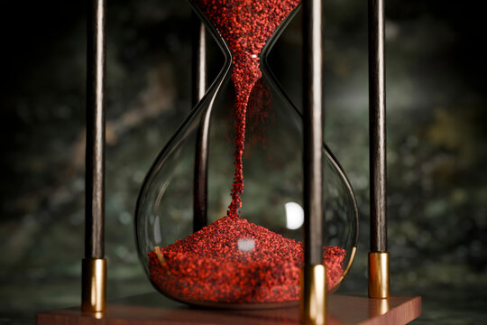 Close-up of a red sand hourglass with a wooden base and black frame.
