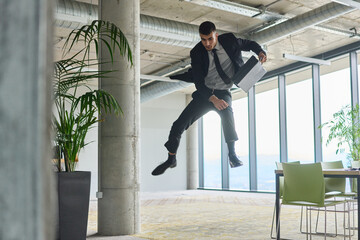 A businessman ecstatically jumping in a modern office, holding a briefcase in his hands,...